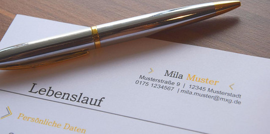 Upper third of a sample CV on paper. You can see the sample address, the German word for CV and the beginning of the personal data category. On top of it is a silver ballpoint pen.