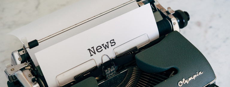 In einer schwarzen, mechanischen Schreibmaschine ist ein Blatt Papier eingespannt, auf dem das Wort "New" getippt ist.