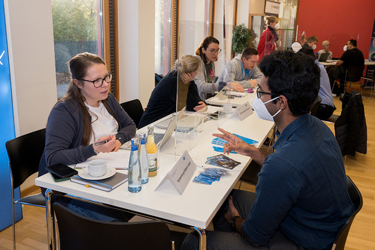An international student in conversation with an employee of a company, both sitting across from each other at a table.